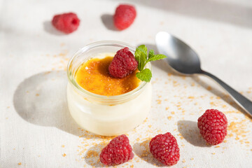 Fresh creme brulee dessert decorated with fresh berries and mint on a linen tablecloth in bright...