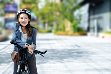 Naklejka premium Young Asian businesswoman wearing helmet and standing on a city street with bicycle looking at phone.