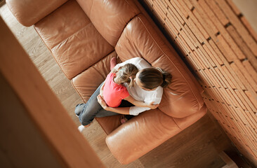 Top view of single mother sitting on the couch at home holding her child daughter. Motherhood, and...