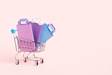 Shopping cart with purple, lilac and blue paper bags on a pastel pink background. Minimalist design...