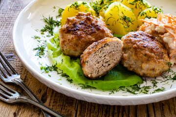 Fried meatballs with boiled potatoes and carrot salad on wooden table
