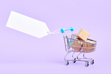 Shopping cart full of boxes with a blank label on a pastel lilac background. Minimalist design with copy space. Concepts: market deals, seasonal sales and discounts, black friday advertising. © Carolina Jaramillo