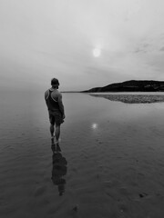 A figure standing on Sandyhills Beach in Scotland at low tide.