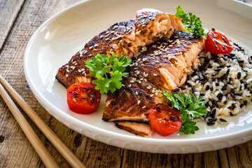 Fried teriyaki salmon steak with black and white rice on wooden table
