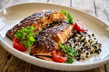Fried teriyaki salmon steak with black and white rice on wooden table
