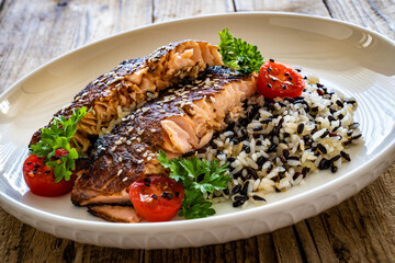 Fried teriyaki salmon steak with black and white rice on wooden table
