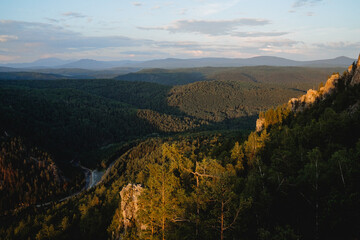 A beautiful landscape of mountains at sunset, the sun illuminates the tops of the trees, the panorama of the river valley, the misty haze over the forest.