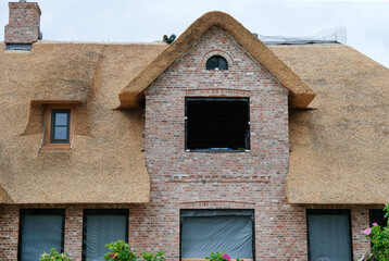 Konzept Hausbau mit Reetdach: Frontansicht der Baustelle eines typisch norddeutschen Klinkerhauses mit frisch eingedecktem Reetdach, selektiver Fokus