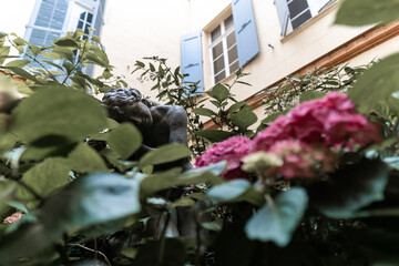 Dark statue hidden  in pink flowers at the middle of a building, in south of france