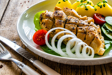 Fried chicken breasts with boiled potatoes and fresh vegetables on wooden table
