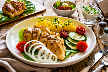 Fried chicken breasts with boiled potatoes and fresh vegetables on wooden table
