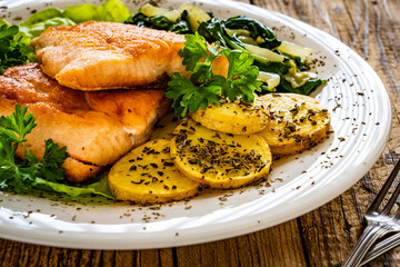 Fried salmon steak with potatoes, spinach and fresh vegetables served on wooden table
