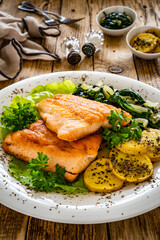 Fried salmon steak with potatoes, spinach and fresh vegetables served on wooden table
