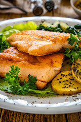 Fried salmon steak with potatoes, spinach and fresh vegetables served on wooden table
