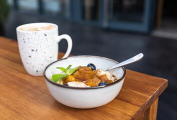 Composition with bowl of oatmeal and coffee in mug on wooden table, open terrace of street cafe. Healthy and tasty breakfast with oatmeal porridge in cafe.