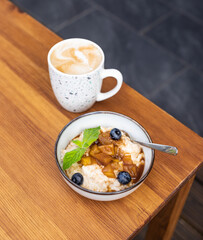 Composition with bowl of oatmeal and coffee in mug on wooden table, open terrace of street cafe. Healthy and tasty breakfast with oatmeal porridge in cafe.