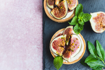 Tartlets pastry with white cream, topped with figs and pistachio, pink background. Cooking concept. Healthy dessert. Top view.