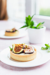 Tartlets pastry with white cream, topped with figs and pistachio on pink background. Cooking concept. Healthy dessert.