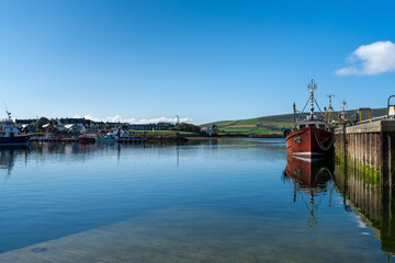 red fishing boat on the docks of Dingle Harbor in County Kerry with reflections in the calm water