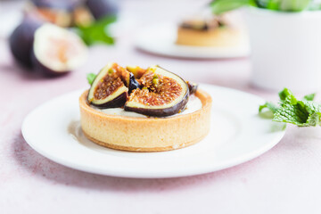Tartlets pastry with white cream, topped with figs and pistachio on pink background. Cooking concept. Healthy dessert.