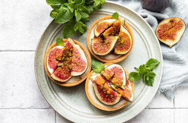 Delicious tartlet with crispy almond-flavored pastry, delicate cheese cream and fresh figs, gray tilled background. Autumn dessert. National Dessert Day, October 14.