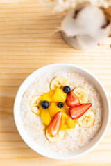 Oatmeal porridge with berries, banana and mango in a bowl on wooden table. Healthy breakfast.