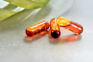 Curcumin in liquid form. Herbal capsules, herb turmeric capsules on neutral background with palm leaf shadow. Herbal medicine extract from turmeric roots. Liquid form of curcumin in tiny oil micelles.