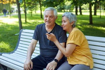 Older couple resting in park seated on bench enjoy talk