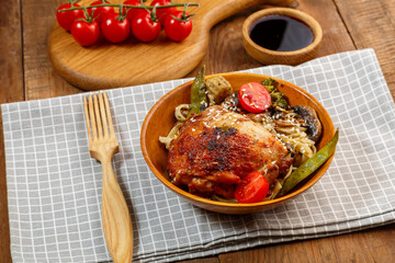 Udon with vegetables and chicken on a table in a wooden plate on a napkin next to tomatoes and a...