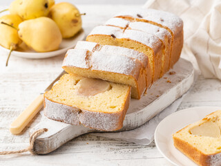 Pear loaf cake sliced on wooden cutting board. Tasty homemade cake baked with whole peeled pears. Seasonal autumn (fall) bakery. Close up view. White wooden table background.