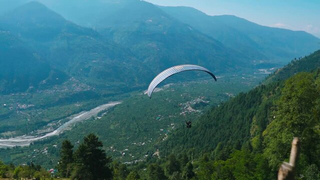 Tourist paragliding on parachute in background of green mountain valley and river during summer at Dobhi ,Manali in Himachal Pradesh. Adventure sports activity in India. 