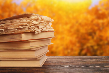 Stack of old books on wooden table outdoors on autumn day