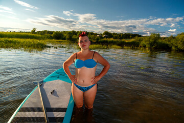 A woman is standing at the sapboard on the shore preparing for swimming.