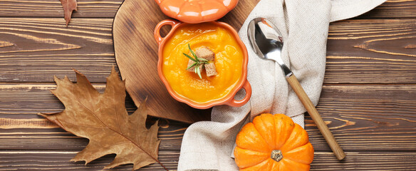Composition with pot of tasty pumpkin cream soup and autumn leaves on wooden background