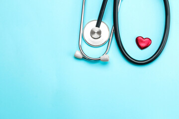 Stethoscope and a small red heart on a blue background. top view and free space. Cardiology and...