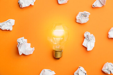Glowing light bulb and crumpled paper on orange background. Concept of idea