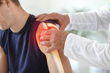 Doctor examining sporty man with pain in shoulder, closeup