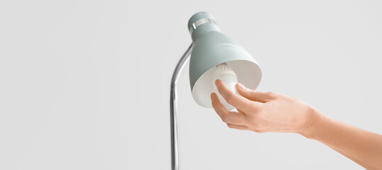 Woman changing light bulb in lamp on grey background