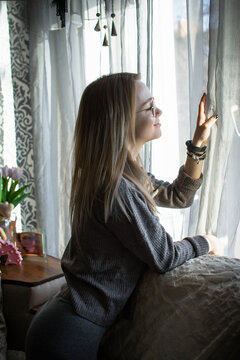 beautiful young woman looks thoughtfully and dreamily out the window at home. Loneliness and melancholy in women