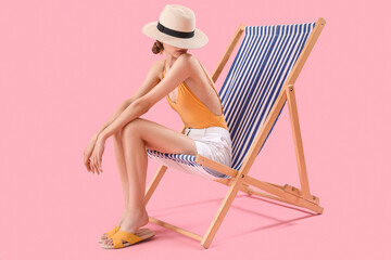 Beautiful young woman relaxing on deck chair against pink background