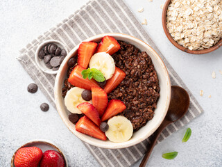 Chocolate oatmeal porridge served with chocolate chips, fresh strawberry and banana slices. Healthy homemade breakfast. Clean eating concept. Vegetarian food. Top view.