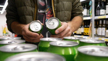 Obraz premium Close-up of many green cans of beer or beverage in alcohol department and a male buyer takes a couple