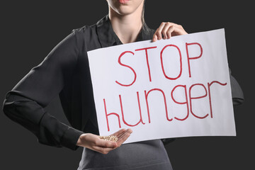 Young woman holding paper with text STOP HUNGER on black background