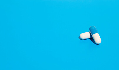 Pharmaceutical industry. Close up of two pills isolated on blue background, painkillers and medicine. White-blue capsules.