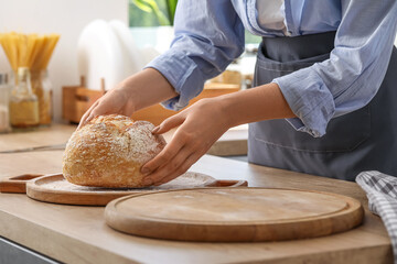 Woman taking fresh bread from board in kitchen, closeup
