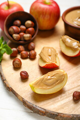 Wooden board of tasty apple wedges with nut butter and hazelnuts, closeup