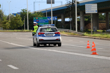 Policjant ruchu drogowego przy swoim radiowozie kontroluje ruch drogowy w mieście.