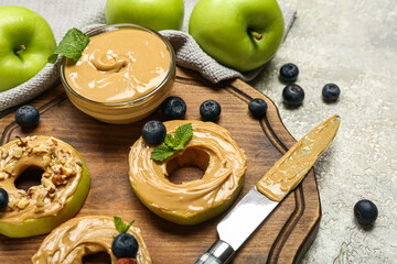 Wooden board of tasty apple rounds with nut butter on light background, closeup