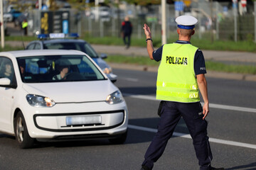 Policjant ruchu drogowego przy swoim radiowozie kontroluje ruch drogowy w mieście. - obrazy, fototapety, plakaty