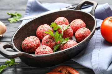 Baking dish with raw meat balls and parsley on dark wooden background, closeup